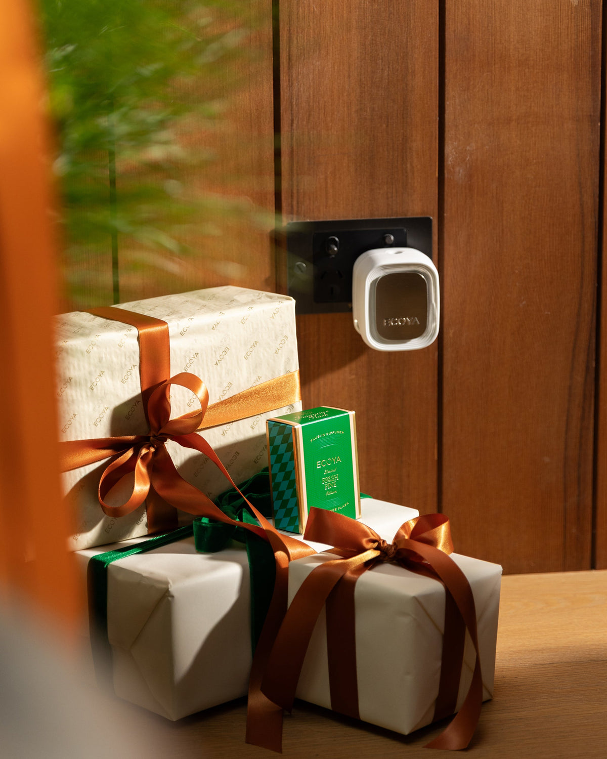 Ecoya plug-in diffuser with the Fresh Pine flask in a wall socket above wrapped gifts