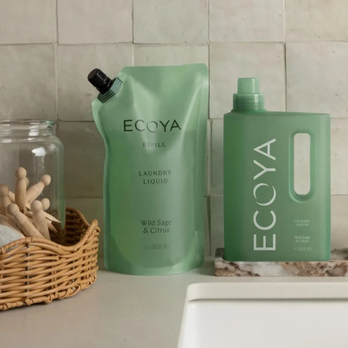 Ecoya Wild Sage and Citrus laundry liquid bottle and refill pouch beside a basket of pegs