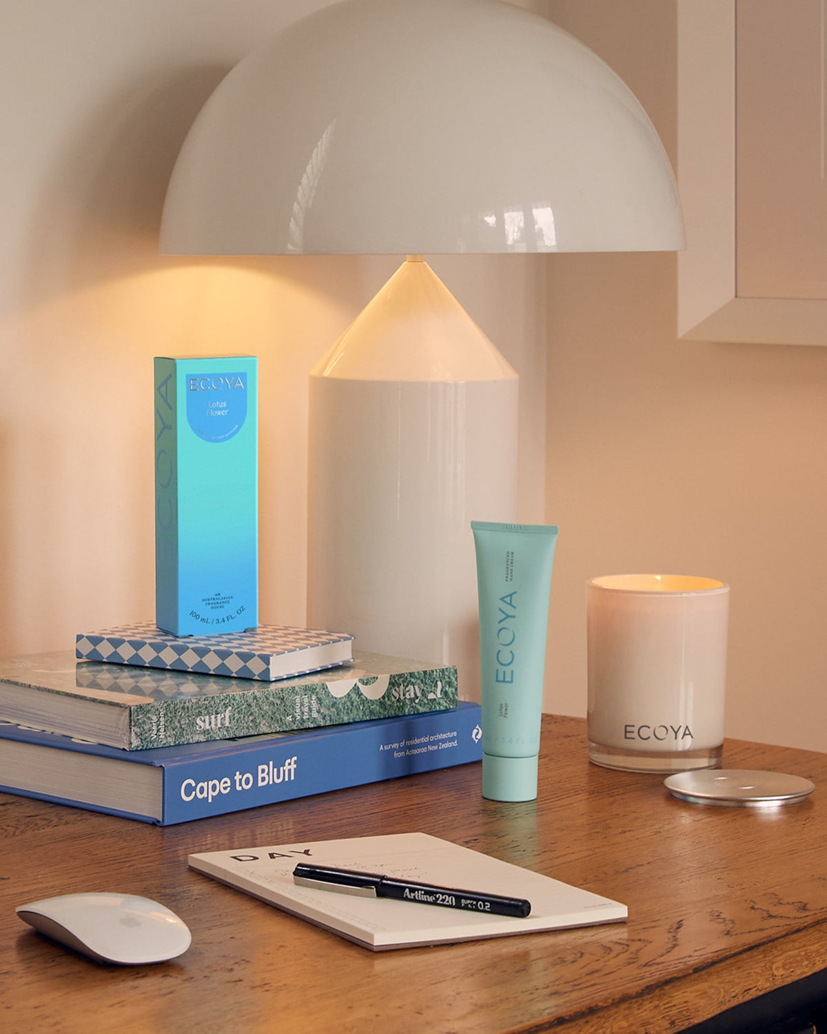 Teal Ecoya hand cream and box on a desk with books and a table lamp