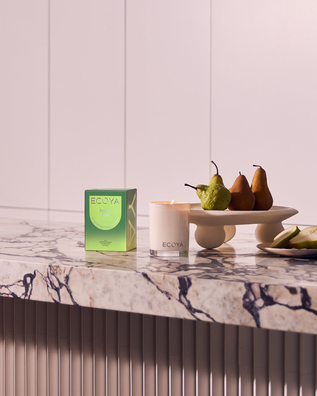 Ecoya Madison candle and its green gift box on a marble benchtop with pears on a pale pedestal stand