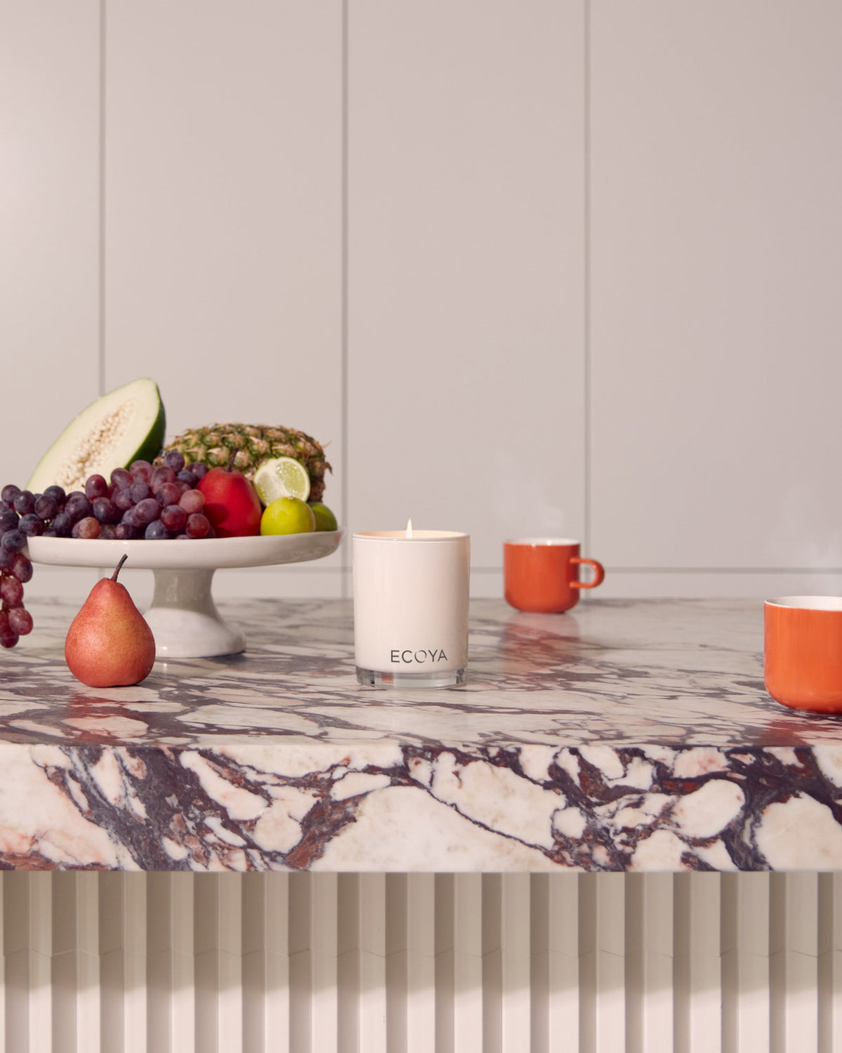 Ecoya Madison candle on a marble console with fruit and a jug against a panelled wall