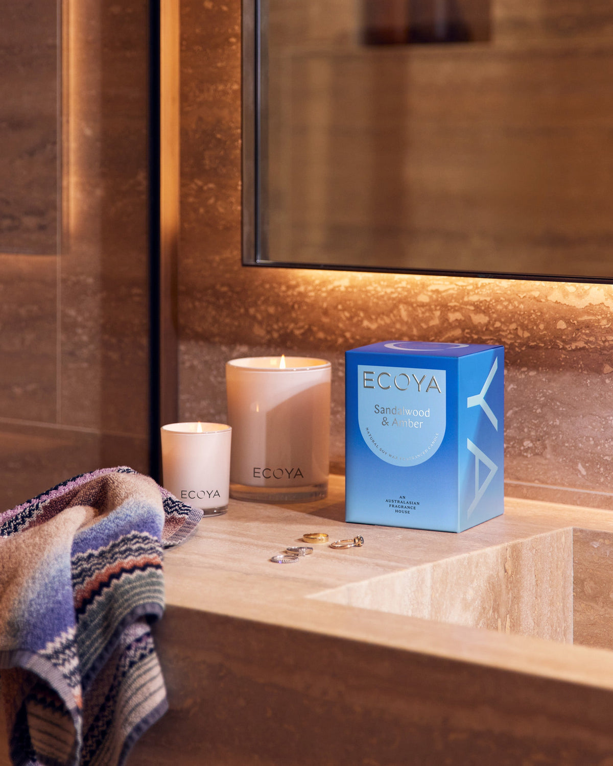 Ecoya Madison candle beside its blue Sandalwood and Amber gift box on a travertine vanity