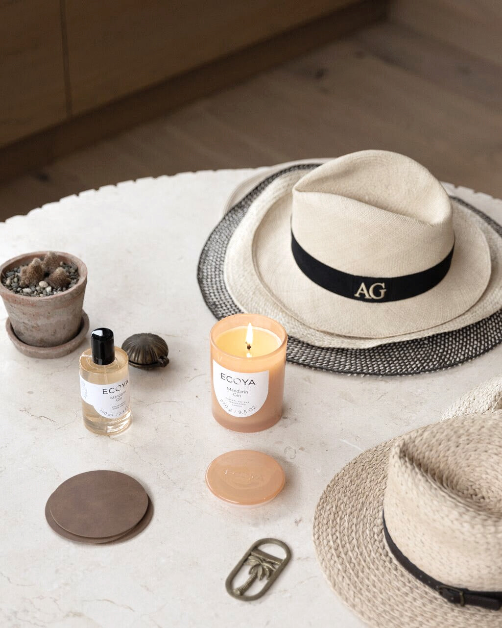 Ecoya room spray and candle on a round marble table with a straw hat and brass keyring