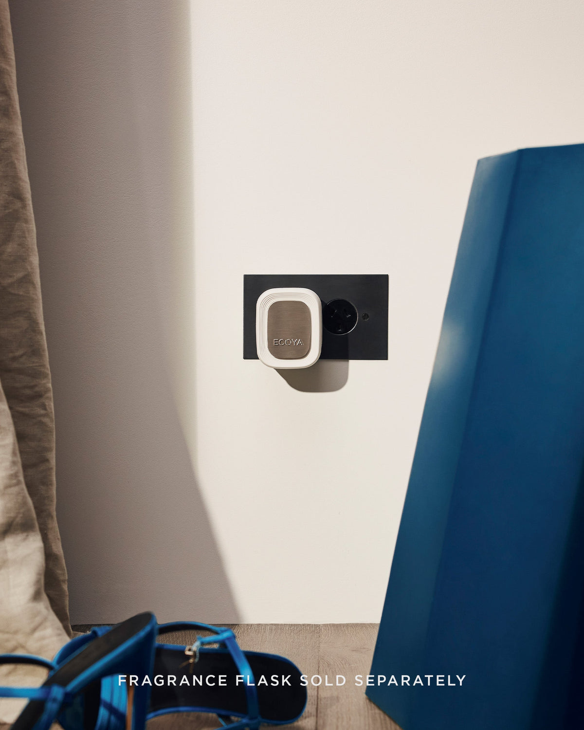Ecoya Plug-In Diffuser in a black socket in a bedroom with a linen curtain and cobalt blue heels
