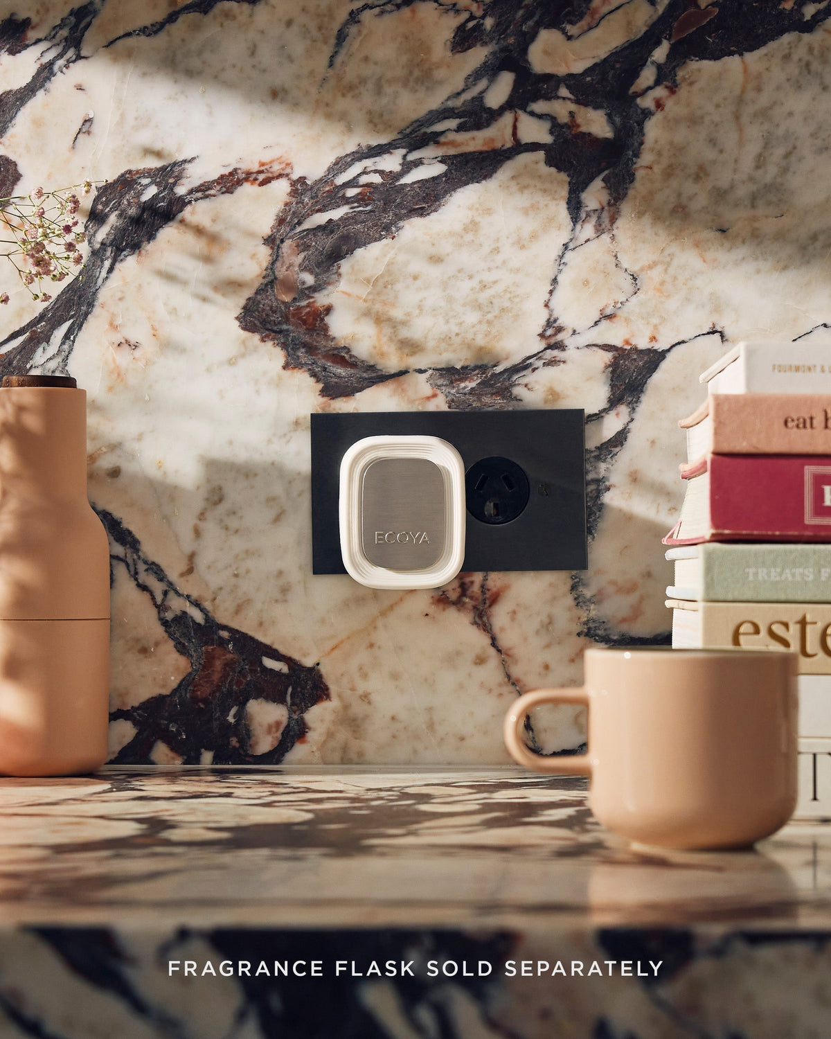 Ecoya Plug-In Diffuser on a marble wall above a kitchen bench with stacked books and a ceramic mug