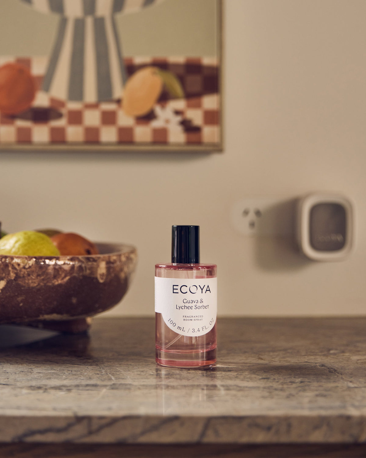 Ecoya plug-in diffuser in a wall socket above a Guava and Lychee Sorbet room spray on a shelf