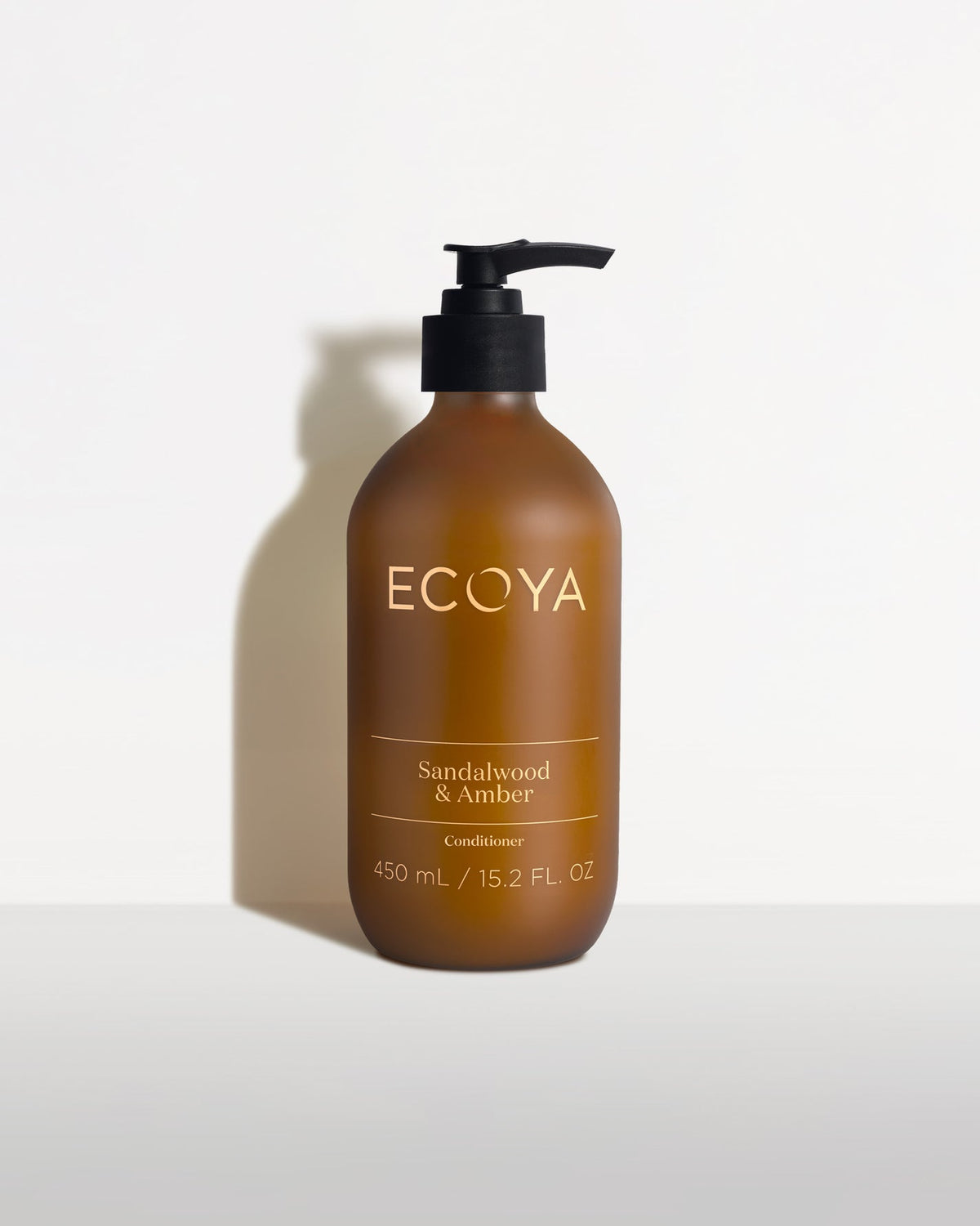 Ecoya Sandalwood & Amber 450ml amber pump bottle casting a soft shadow on a pale background