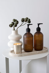 Ecoya Sandalwood and Amber shampoo and conditioner in amber pump bottles on stone tray with candle and vase