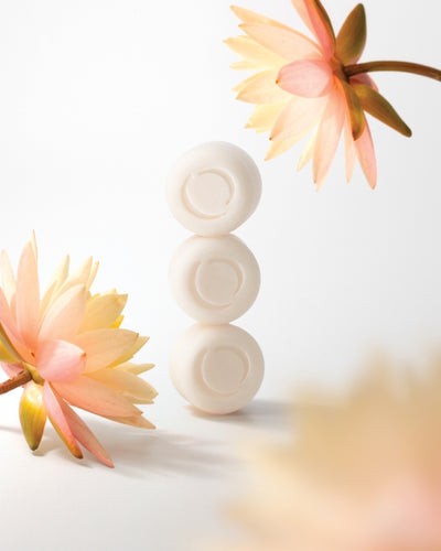 ECOYA Soy Wax Melt discs in Lotus Flower Fragrance stacked beside soft pink lotus flowers on a warm neutral background.