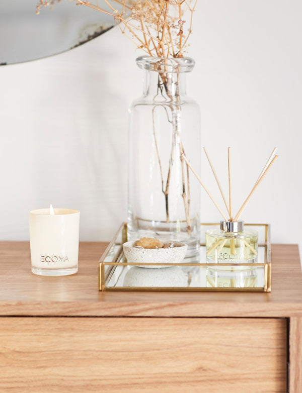 Ecoya Sweet Pea & Jasmine mini candle and diffuser styled on a wooden bedside table with a glass vase and mirrored tray.