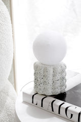 Petite Elara Glow USB LED lamp with a white globe shade and speckled cream base, styled on a round side table on top of a book