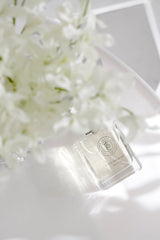 Minimalist flatlay of Elegance roll-on perfume oil bottle on a white surface with soft white florals and sunlight.