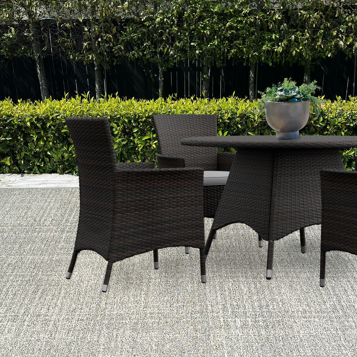 Flecked outdoor rug under dark wicker chairs and a round table on a patio with a hedge behind
