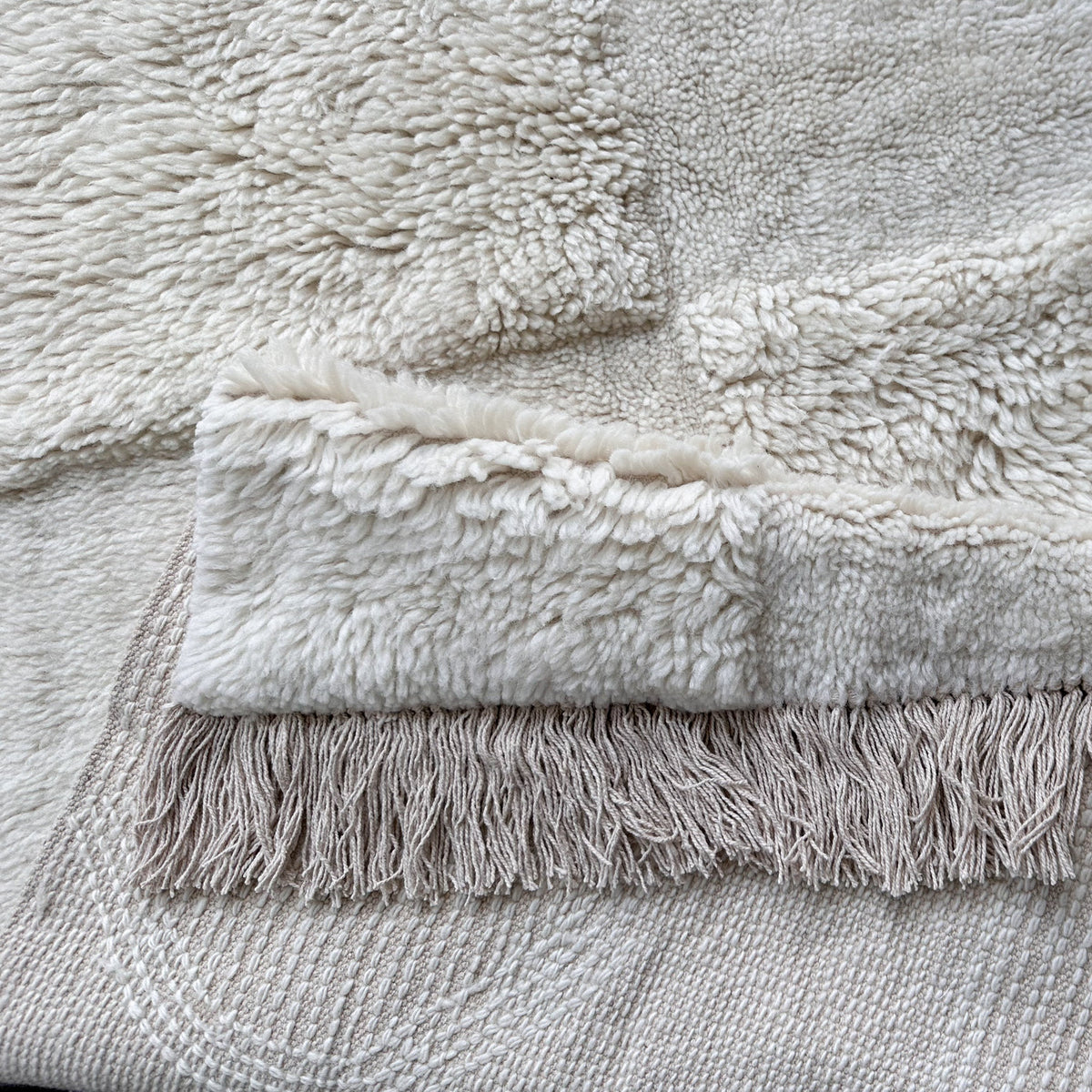 Ivory wool rug folded over to show its fringed end and backing