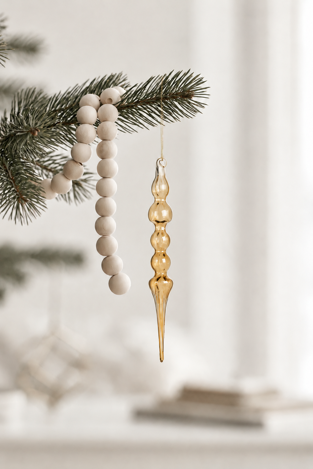 Ethereal glass finial in clear gold hanging from a pine branch beside a wooden bead garland