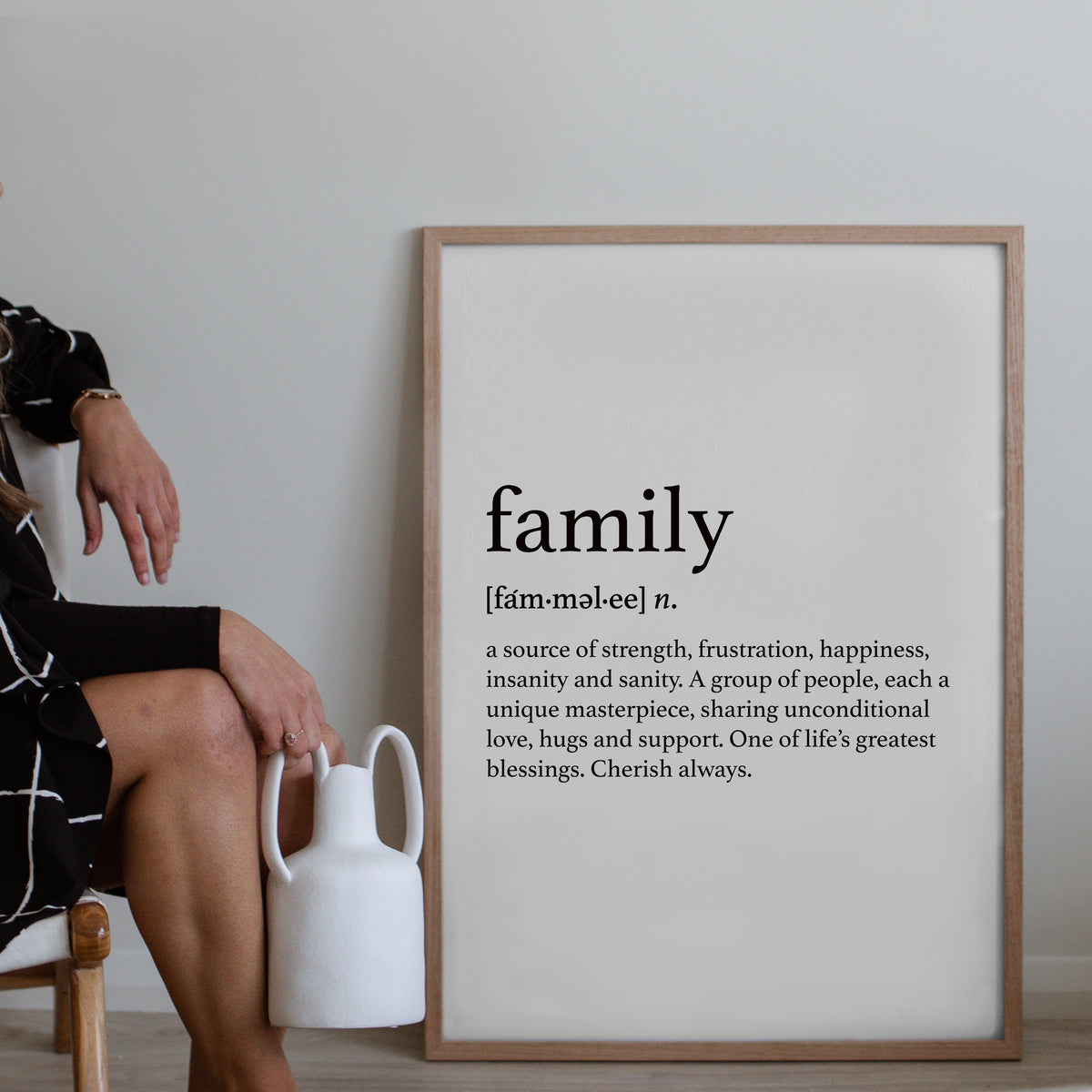 Family print in a natural frame leaning against a wall beside a white vase
