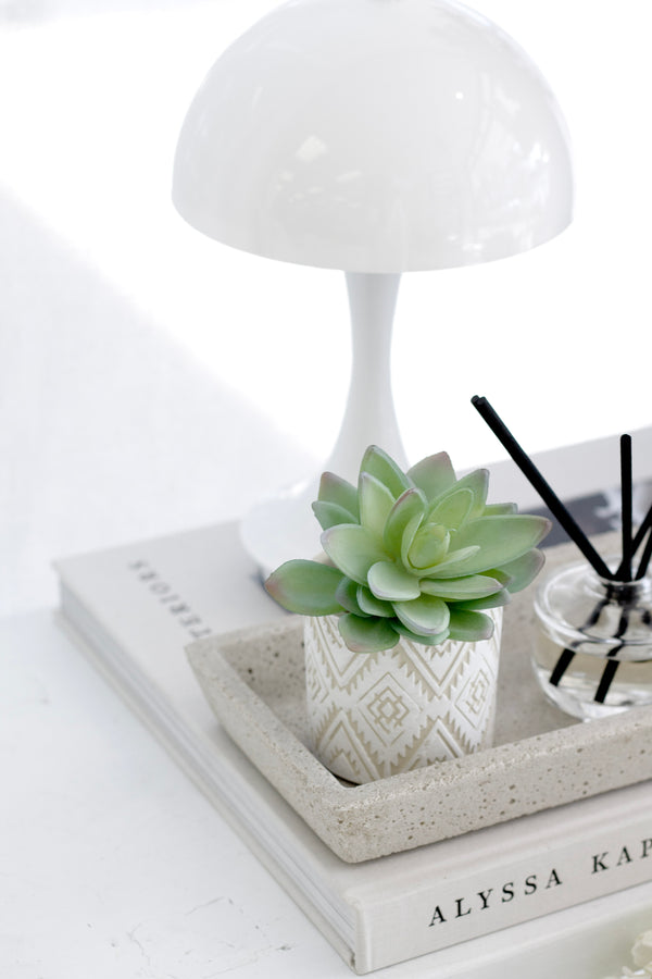 Mini faux lotus succulent with soft green leaves and grey tips styled in a white pot on a stone tray with books and a diffuser.