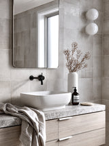 Faux Talinum spray stem in white ribbed vase styled on marble bathroom vanity with matte black tapware and globe wall lights