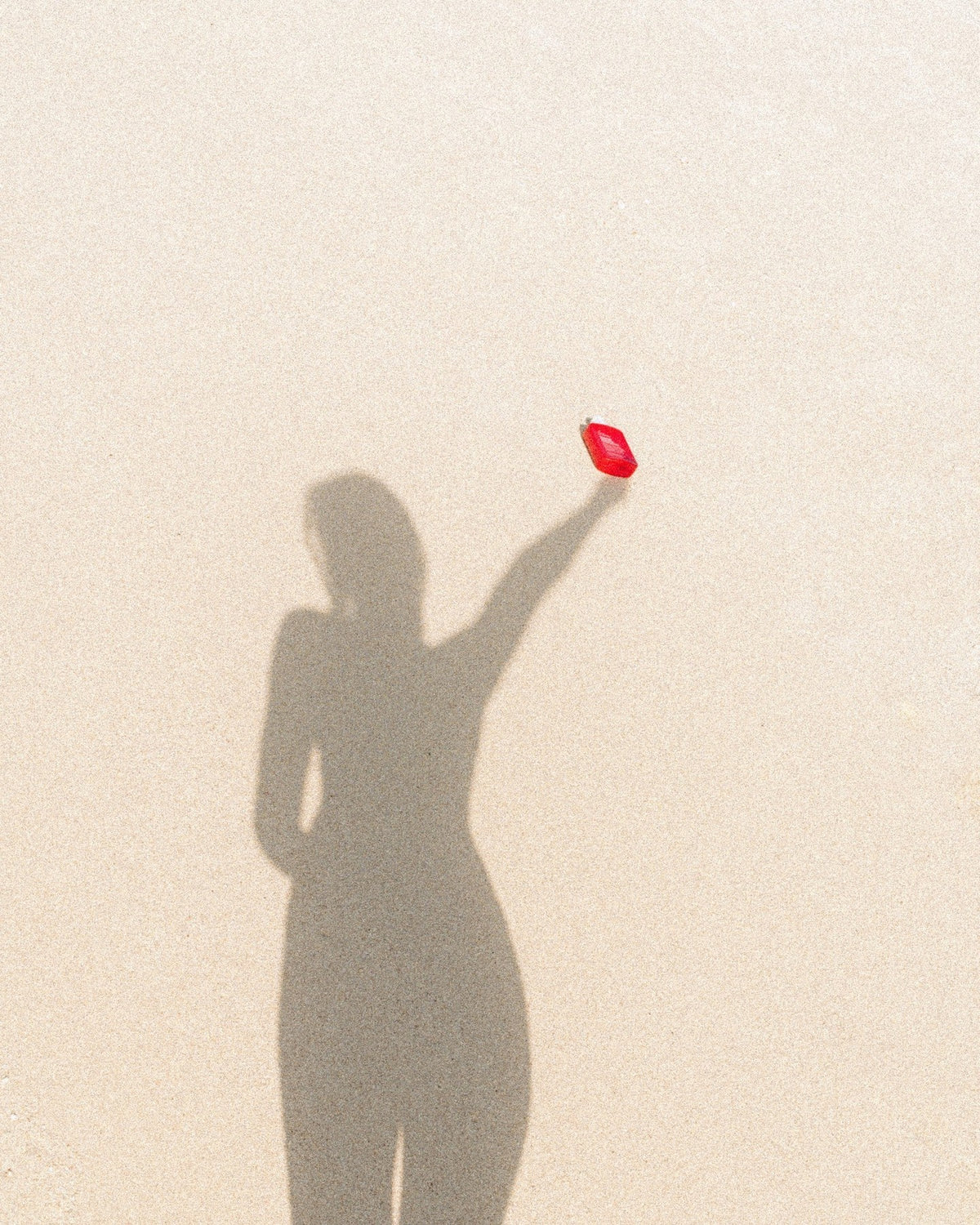 Feel Good Inc Signature Sunscreen SPF 50+ held against sandy background with shadow of person who appears to be holding the sunscreen bottle in the air