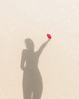 Feel Good Inc Signature Sunscreen SPF 50+ held against sandy background with shadow of person who appears to be holding the sunscreen bottle in the air