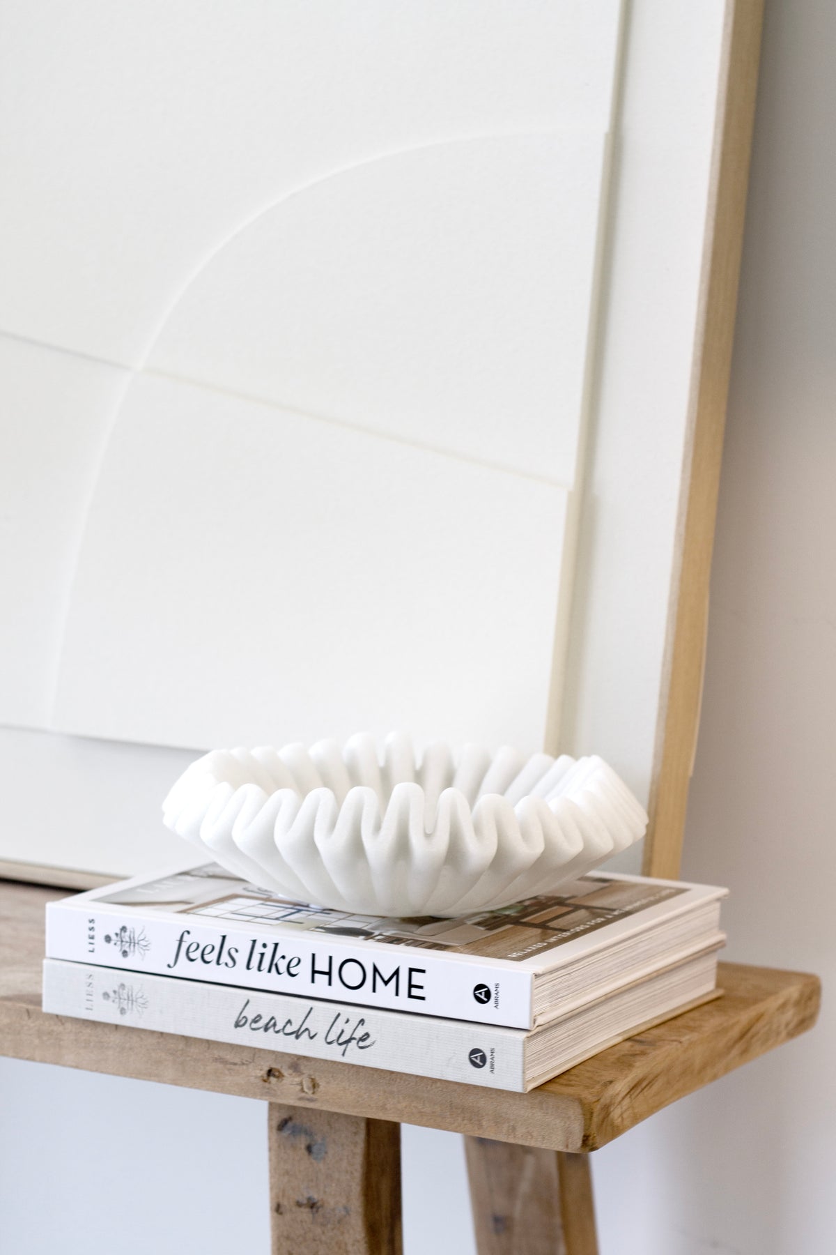 Feels Like Home and Beach Life design books stacked on a timber stool, styled with a white sculptural bowl in a relaxed coastal home