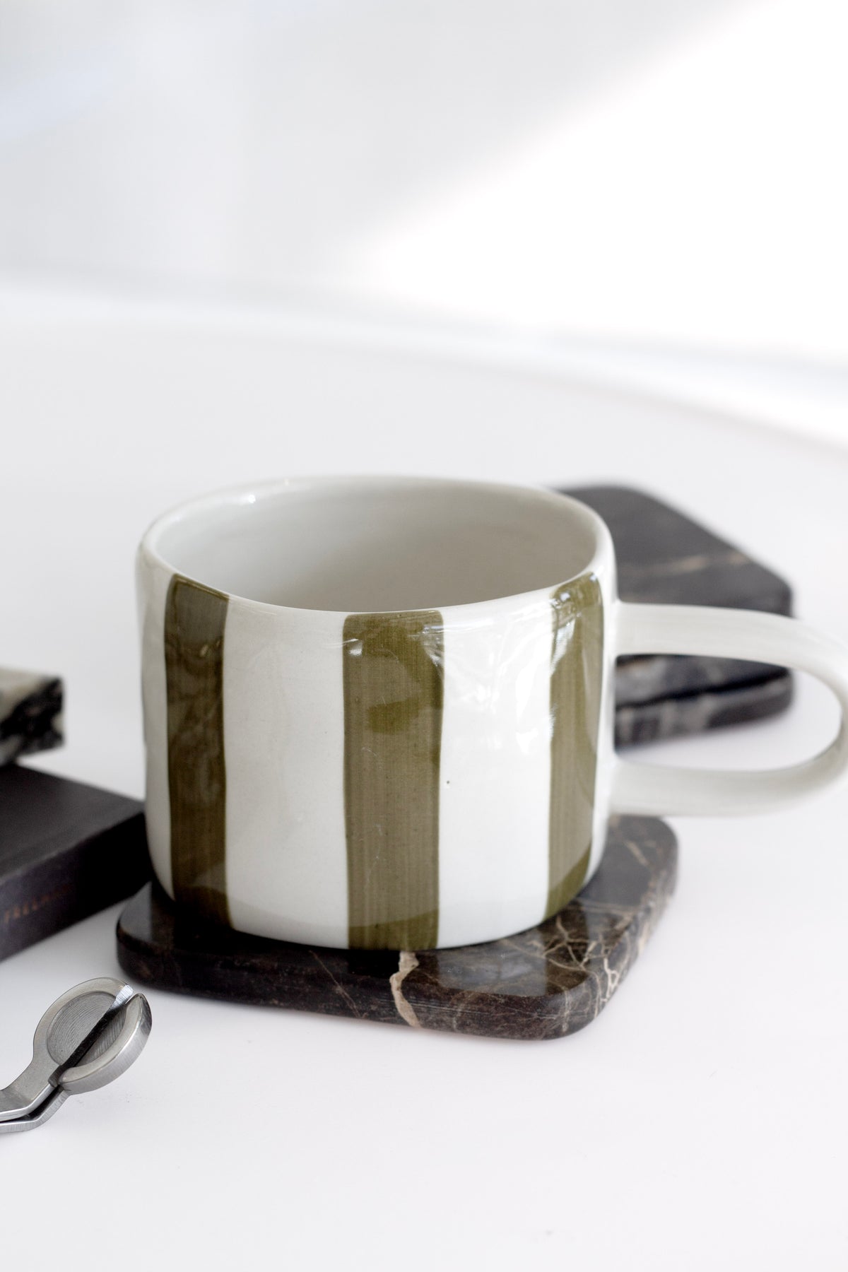 Fenton Stripe Mug in stoneware with hand-painted olive green and white organic stripes, styled on marble coaster with modern kitchenware.