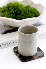 Neutral ceramic tumbler on dark marble coaster styled on coffee table book with decorative bowl