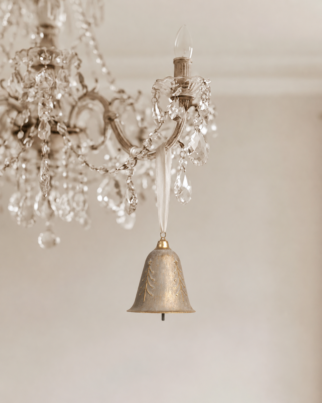 Filigree bell in brushed champagne hanging on a cream ribbon from a crystal chandelier