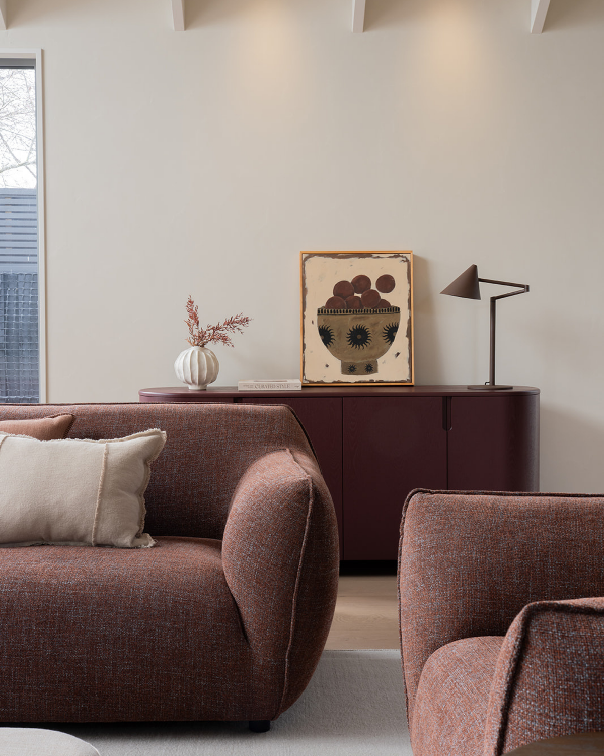 Living room with rust sofas and an oxblood sideboard holding the Coffee Brown lamp, a print and a ribbed vase