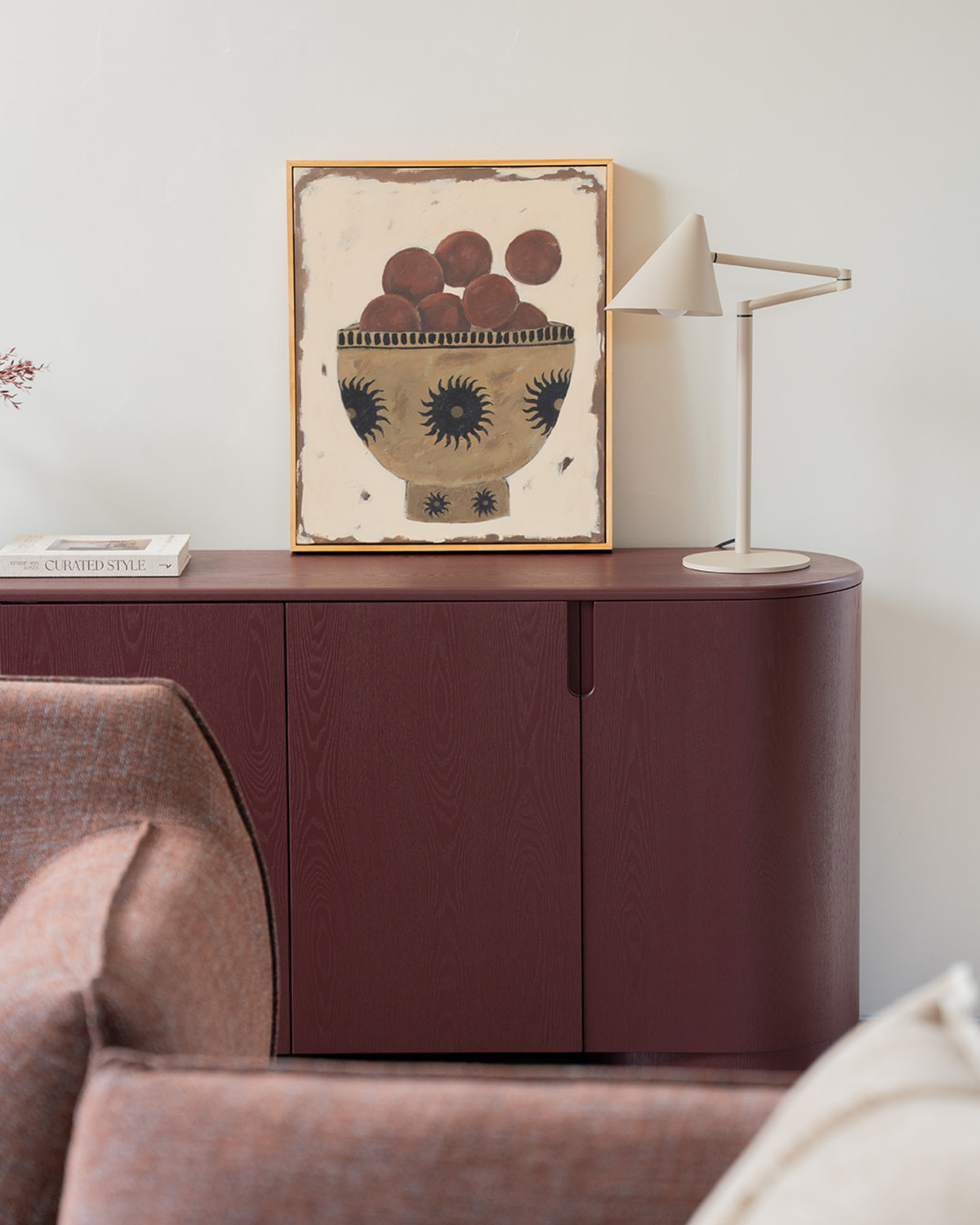 Oat lamp on an oxblood sideboard beside a framed still life print of a fruit bowl