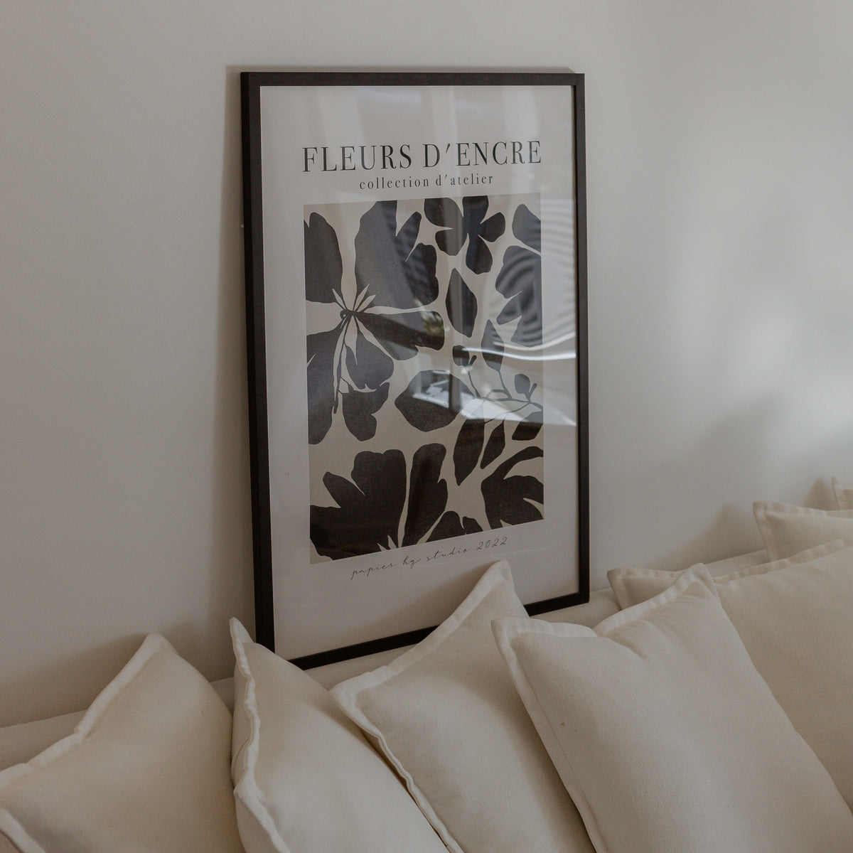 Fleurs d'Encre print in a black frame leaning on a cream sofa with linen cushions