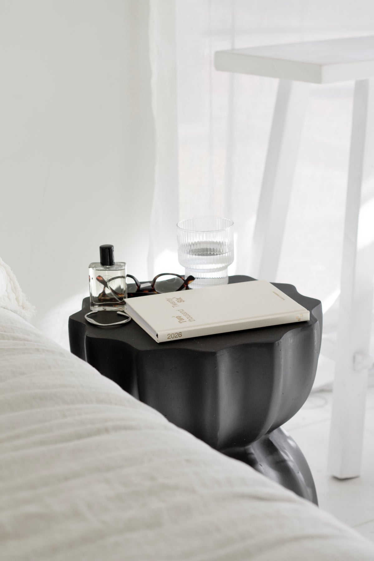 Black fluted table used as a bedside, holding a diary, glasses and a ribbed tumbler