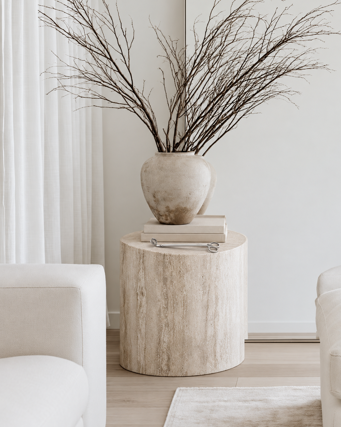 Ecoya Daily Ritual stainless steel wick trimmer lying on a travertine side table beside stacked books and a stone vase