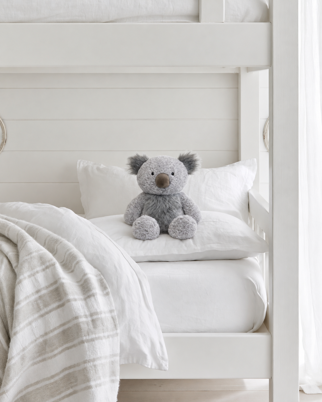 Kenny Koala soft toy by Lily & George sitting against the pillow on the lower bunk of a white bunk bed