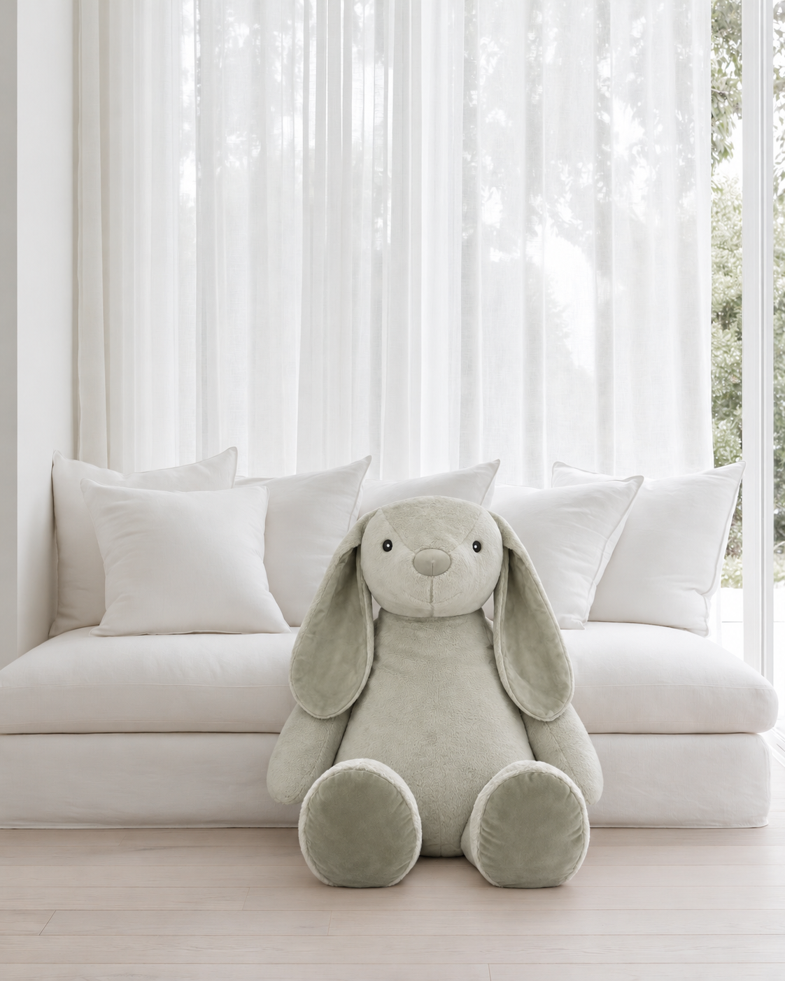Giant Flopsy Bunny in Jade by Lily & George sitting on the floor in front of a low white daybed piled with cushions