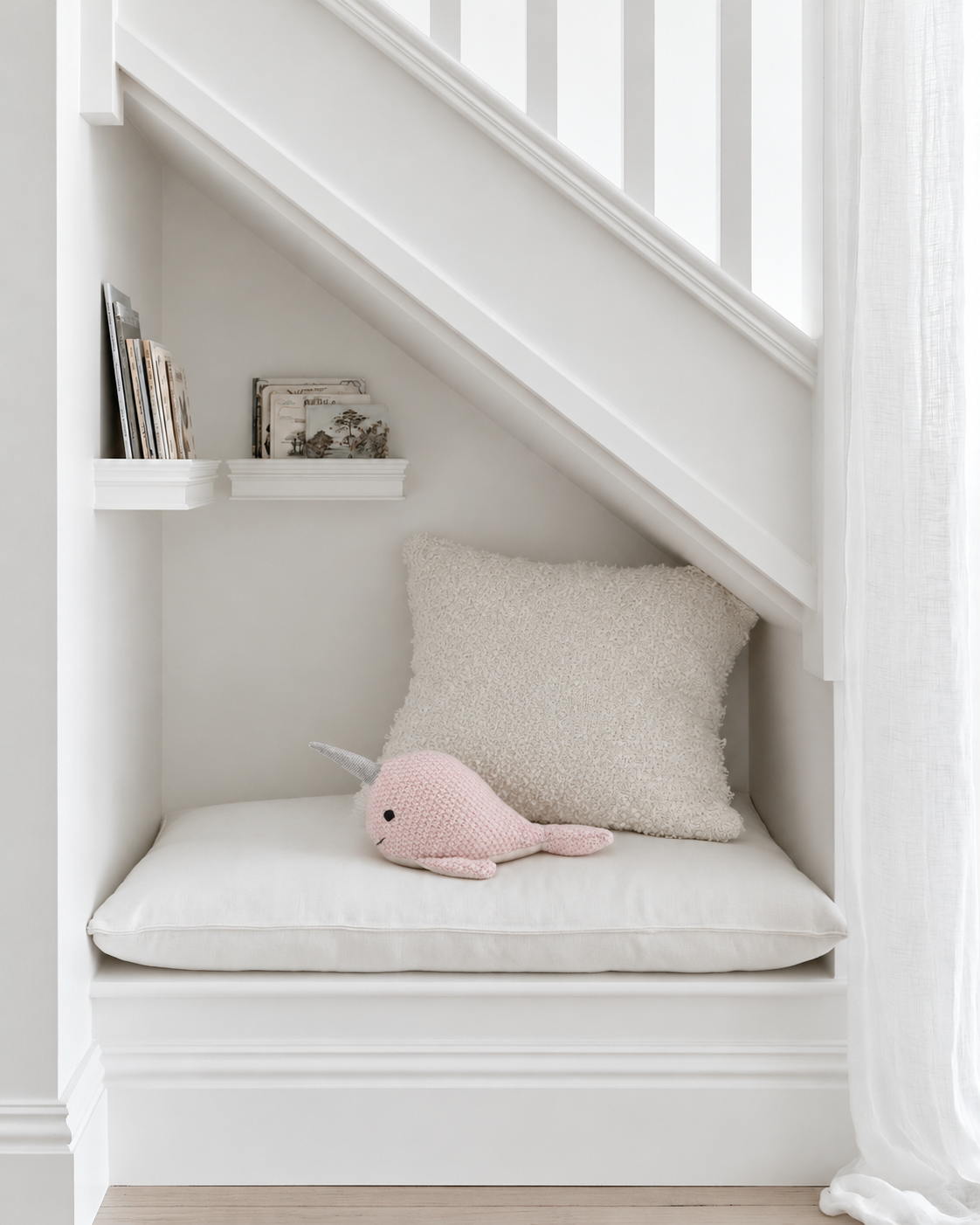 Nellie Narwhal knitted rattle by Lily & George lying on a cushioned reading nook under the stairs