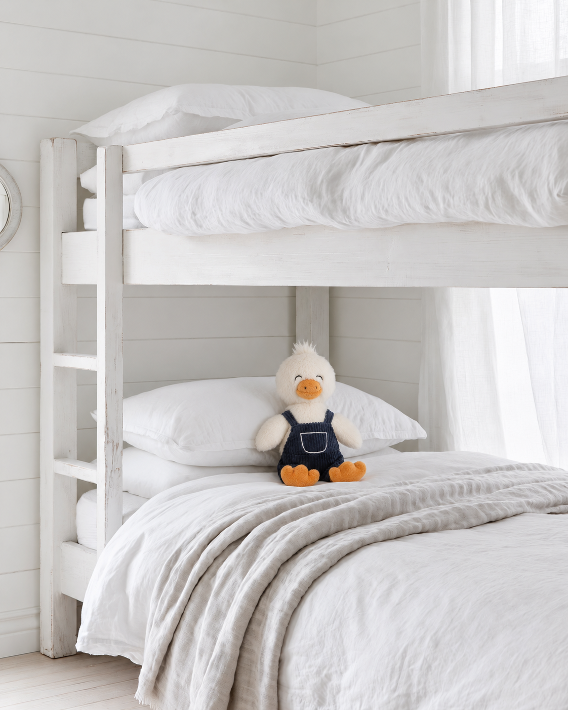Willow the Duck soft toy by Lily & George in navy corduroy overalls sitting on the lower bunk of a white bunk bed