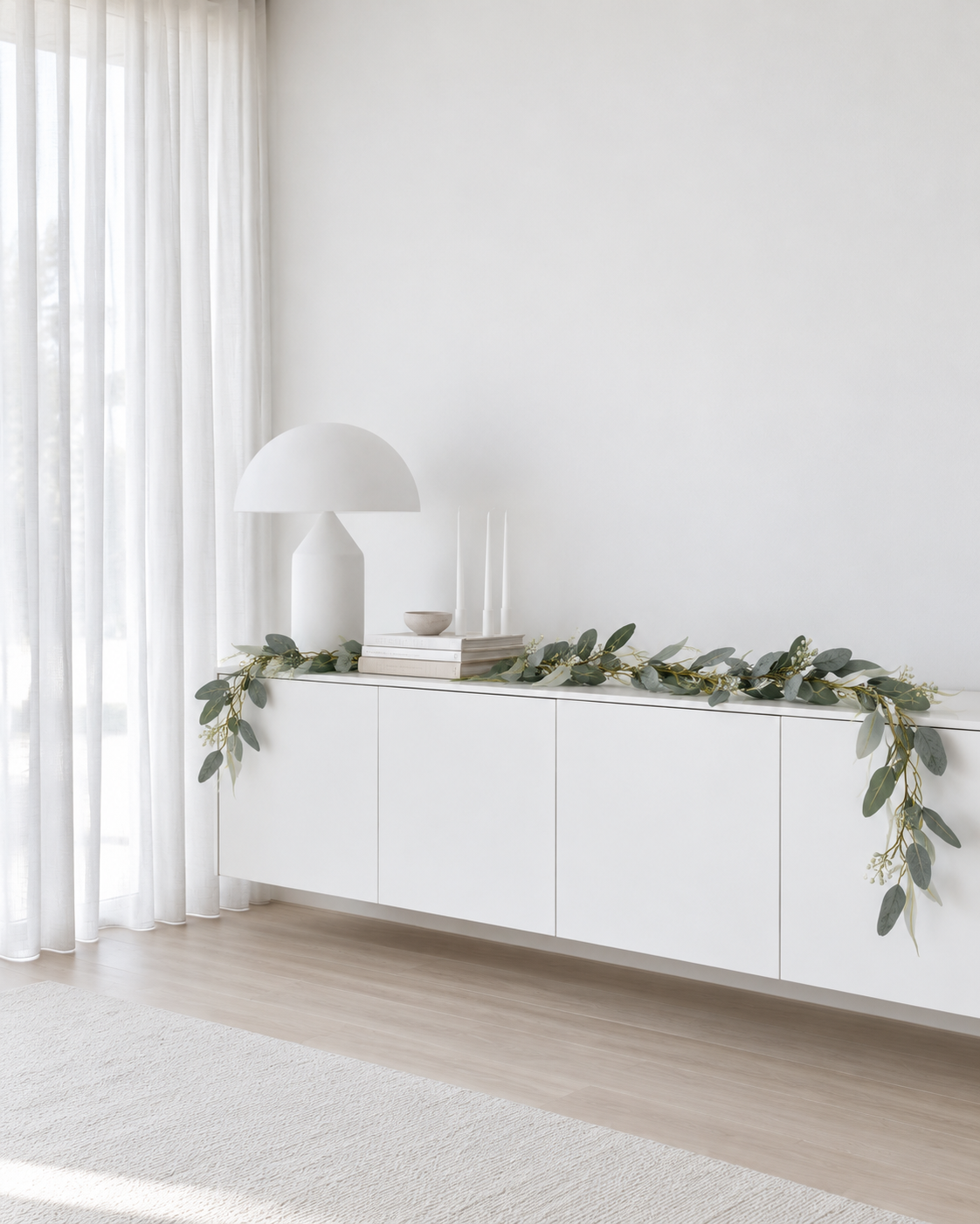 Seeded eucalyptus garland laid along the top of a low white sideboard beside a white mushroom lamp