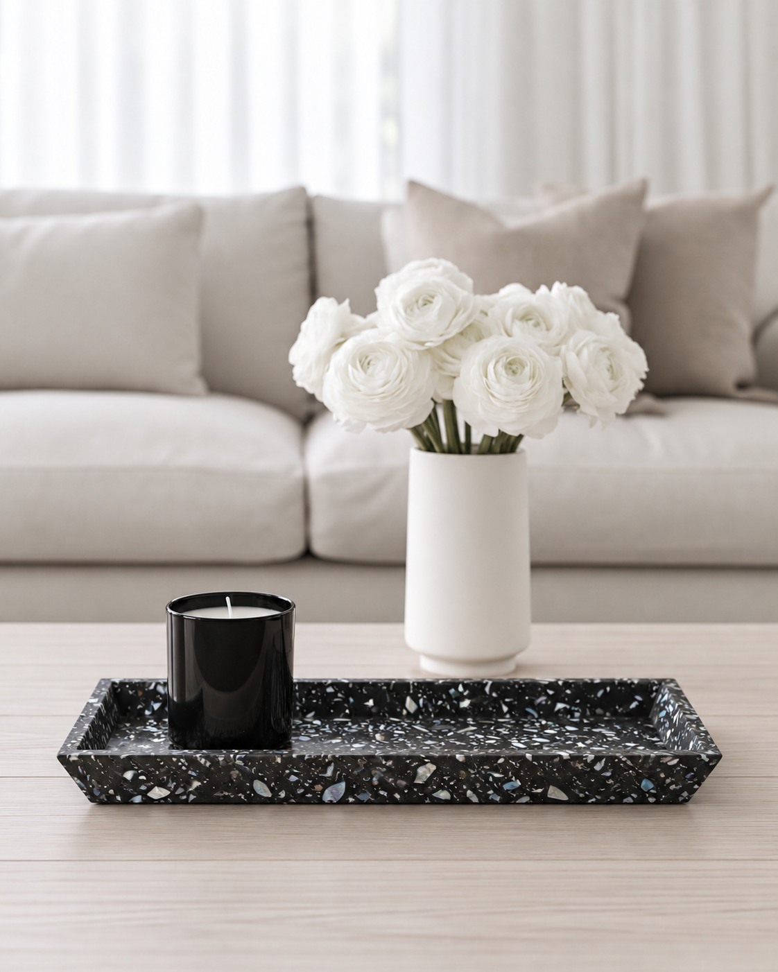 Black seashell terrazzo tray with a candle on a coffee table in front of a linen sofa