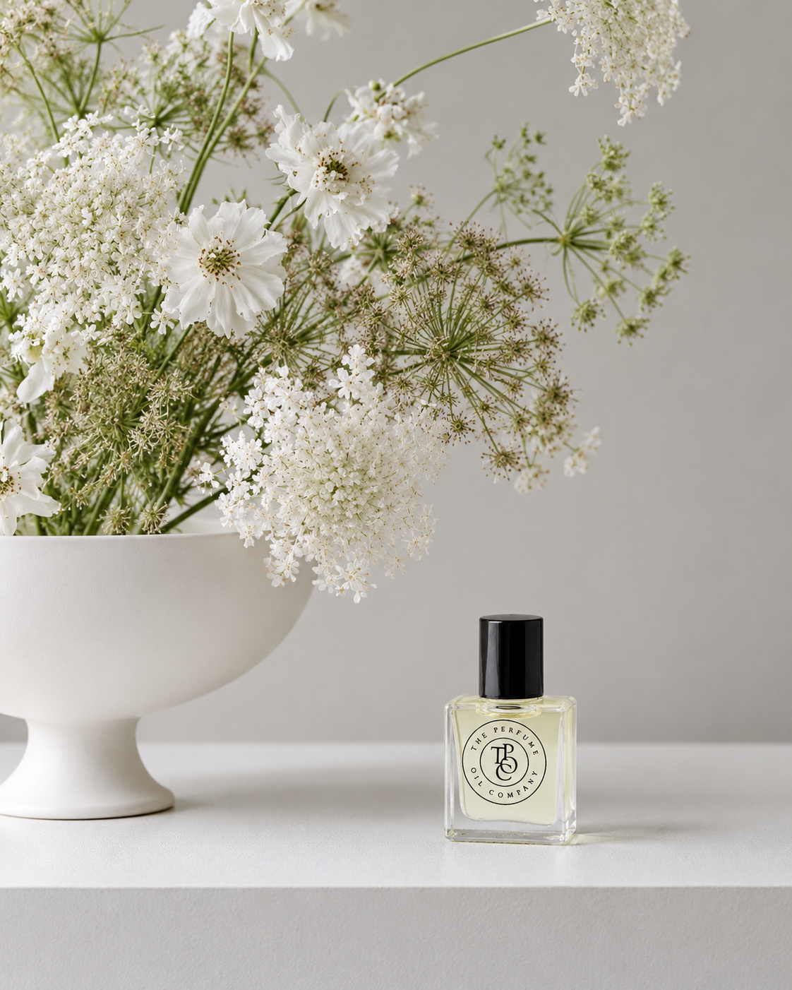 JEWEL Perfume Oil on a white plinth beside the bowl of white flowers