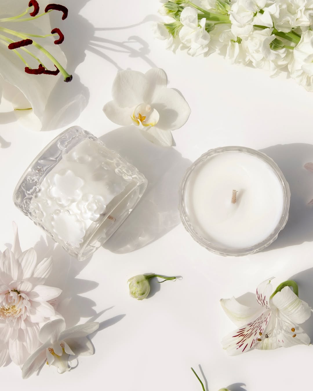 Flat lay of two FLWR candles in embossed glass, one on its side, among white orchids and blooms
