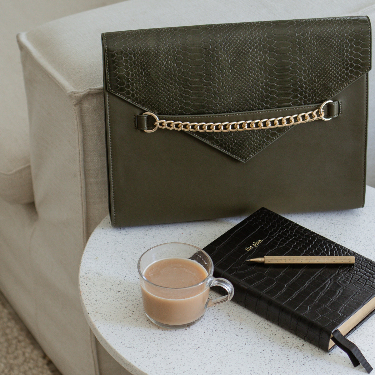 Forest Green laptop sleeve on a side table beside a coffee and notebook