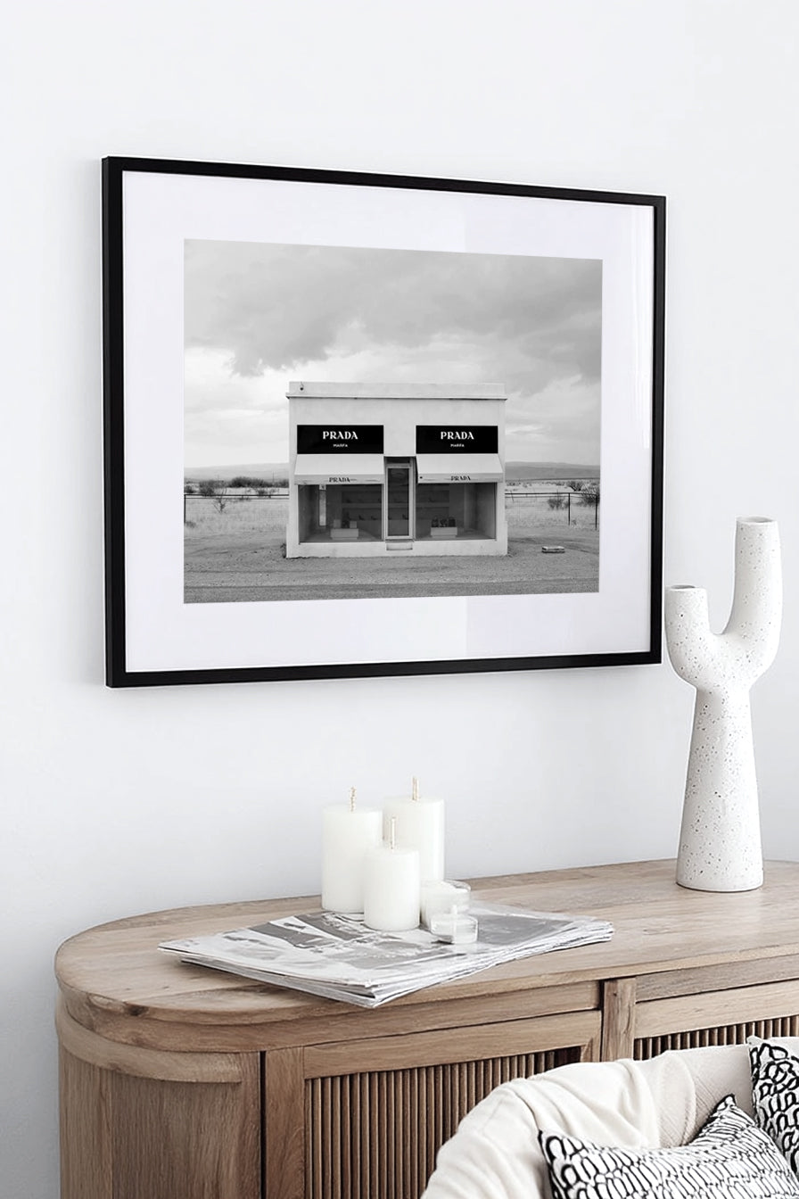Framed black and white print above a timber console with a white sculptural vase, candles and books