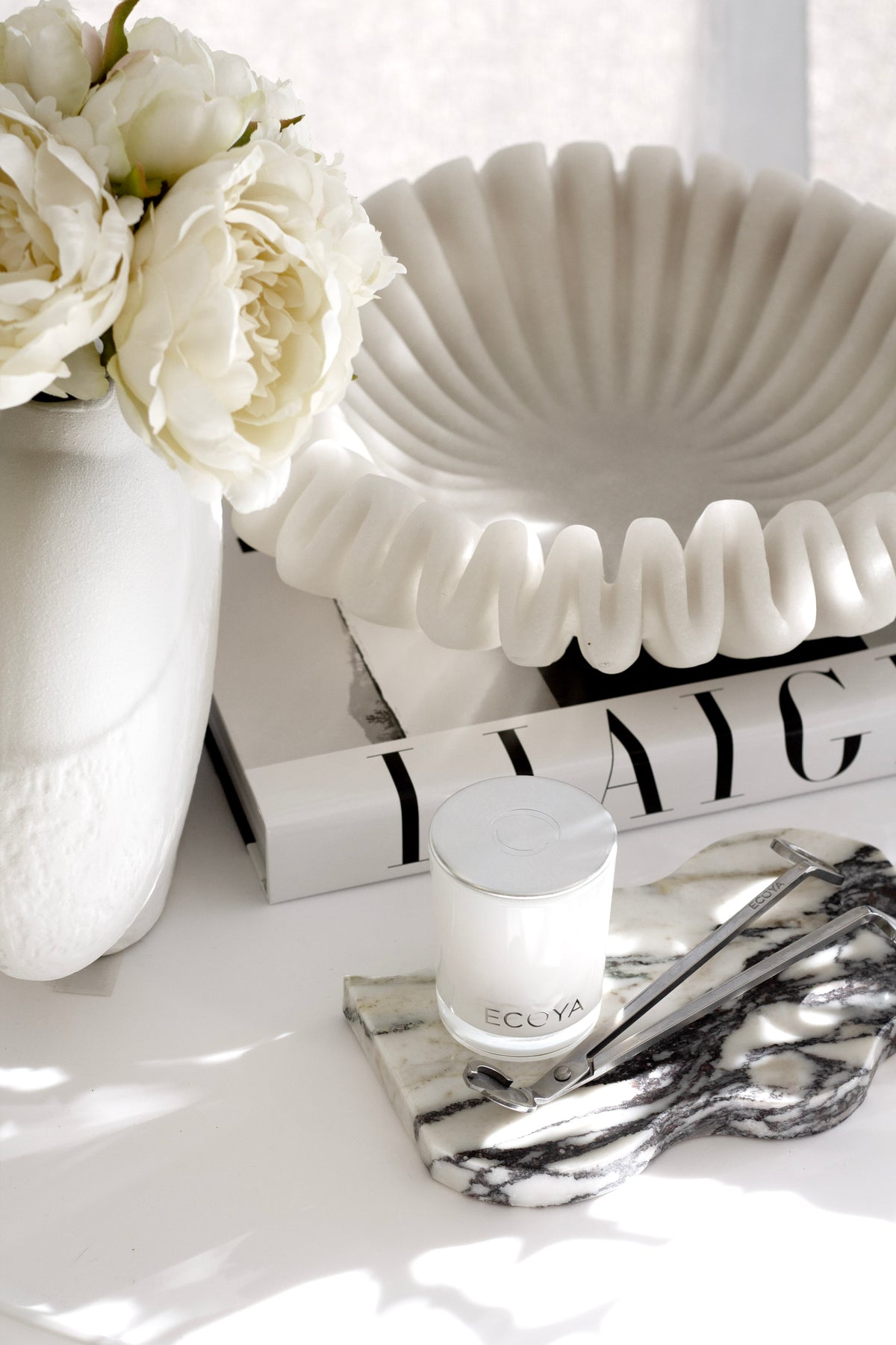 Frida Wavy Tray in Calcutta marble styled with candle, flowers, and coffee table books – modern luxury home decor accent.