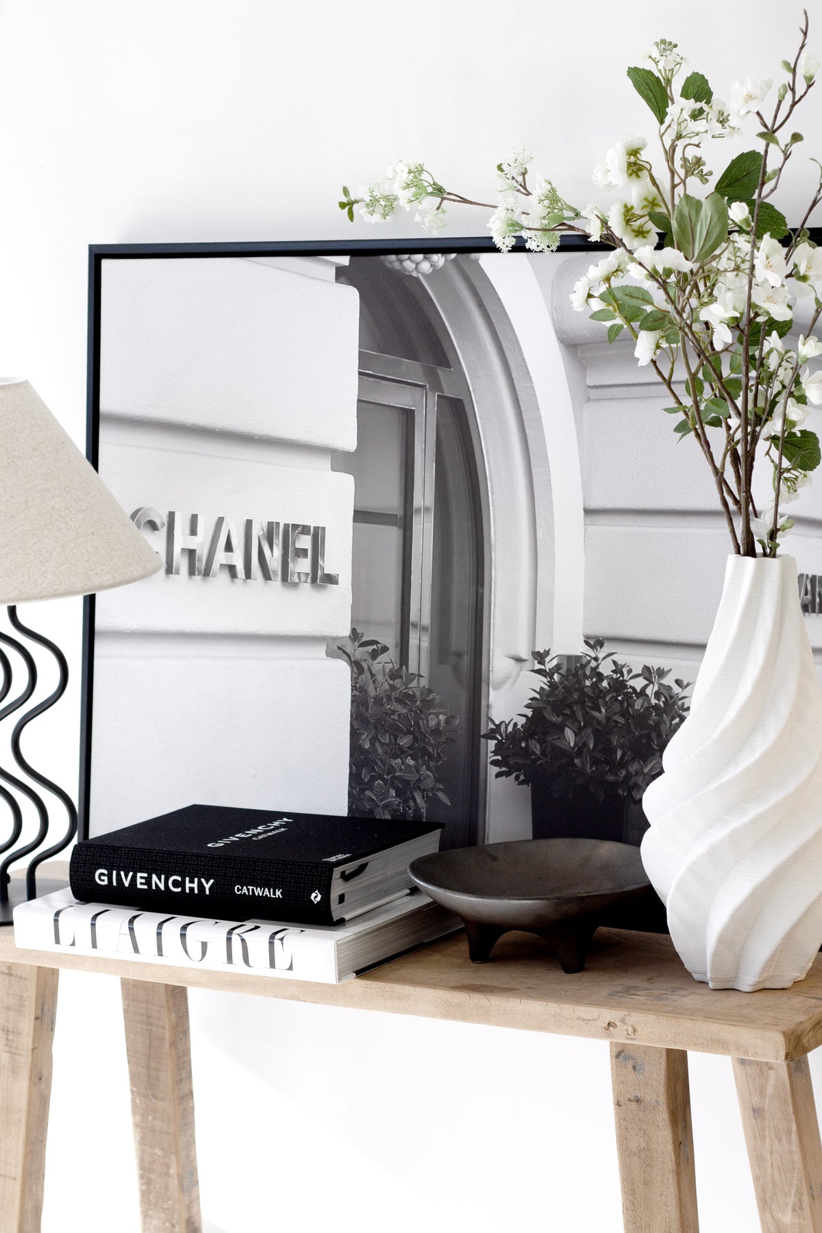 Spiral vase of blossom stems on a timber console with a framed print and stacked books