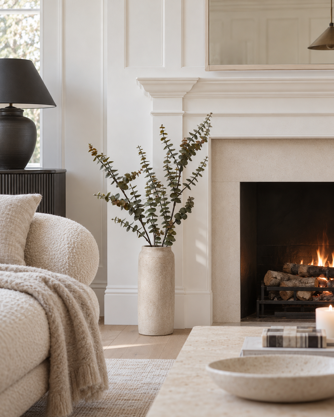 Hinterland gum faux eucalyptus stems arching from a tall stone floor vase beside a fireplace