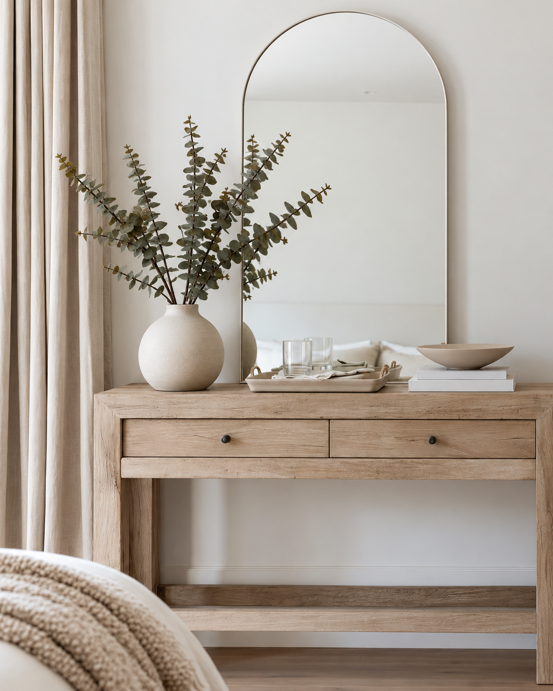 Hinterland gum faux eucalyptus stems in a round stone vase on an oak console below an arched mirror