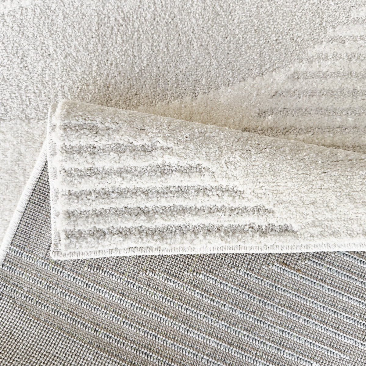 Folded corner of the cloud white rug showing the woven grey backing