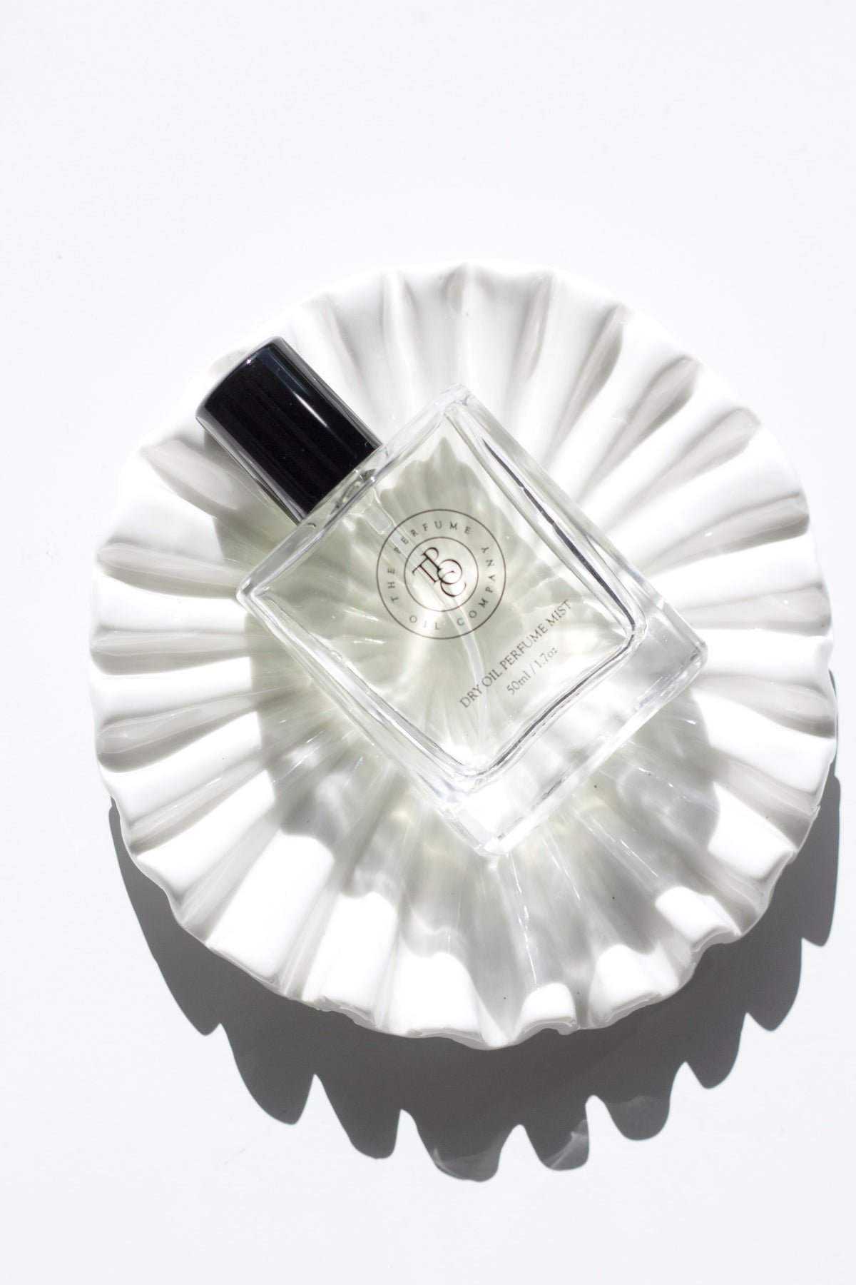 Perfume oil bottle on a white rippled ceramic dish, seen from above