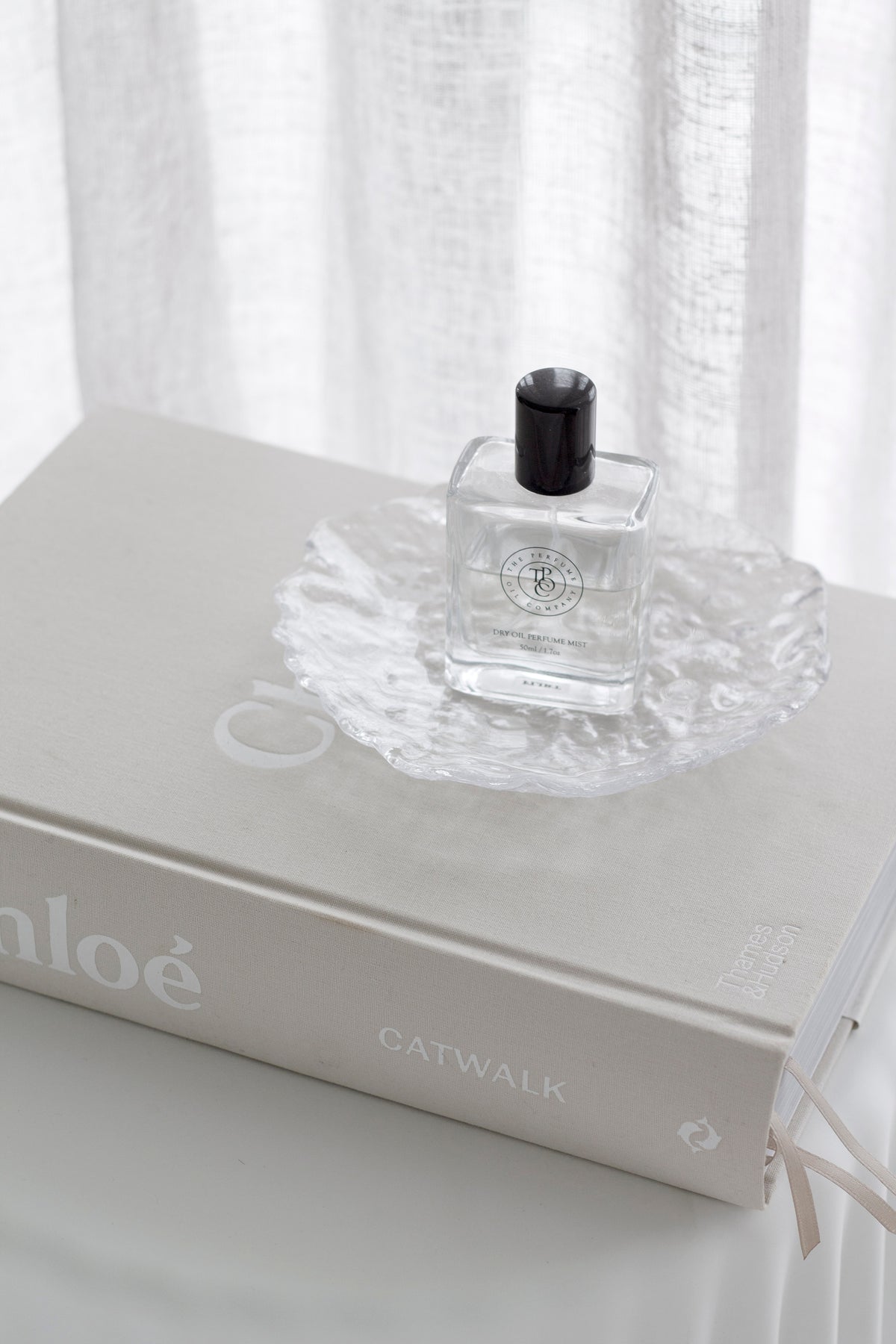 Glacier glass tray holding a small perfume bottle on a stack of books